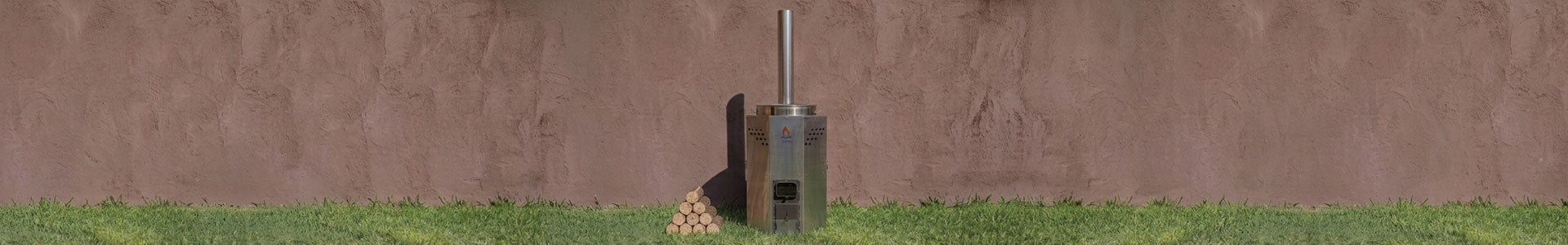 An SSM institutional stove with a vertical chimney stands on grass next to a stack of briquettes against a textured brown wall.
