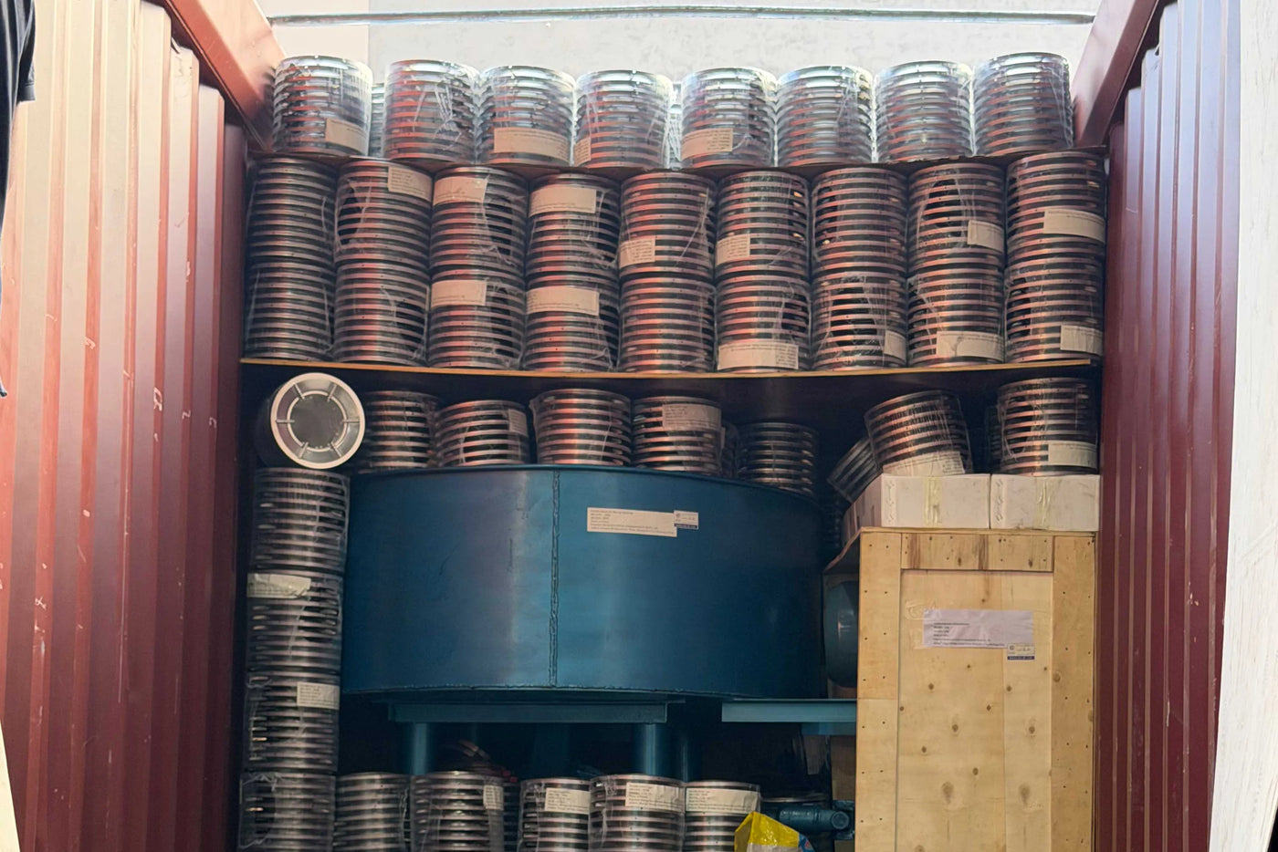 A shipping container tightly packed with neatly stacked stacks of biomass stove parts and components, including wrapped stainless steel combustion chambers, stove bodies, and a wooden export crate, prepared for international export at Zhejiang Huiwenmei Stove Co., Ltd. (SSM).