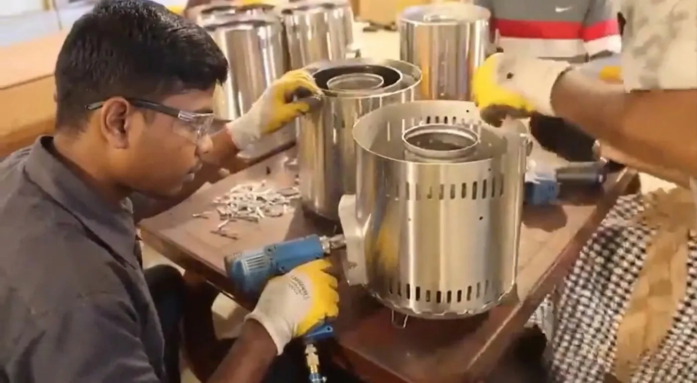 Local assembly workers wearing protective gloves and working together around a table to assemble stainless steel biomass cookstoves at SSM's local assembly project site in Sri Lanka.
